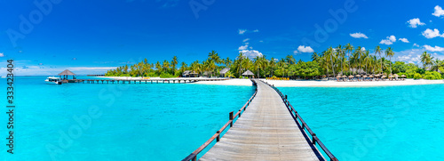 Maldives island beach panorama. Palm trees and beach bar and long wooden pier pathway. Tropical vacation and summer holiday background concept