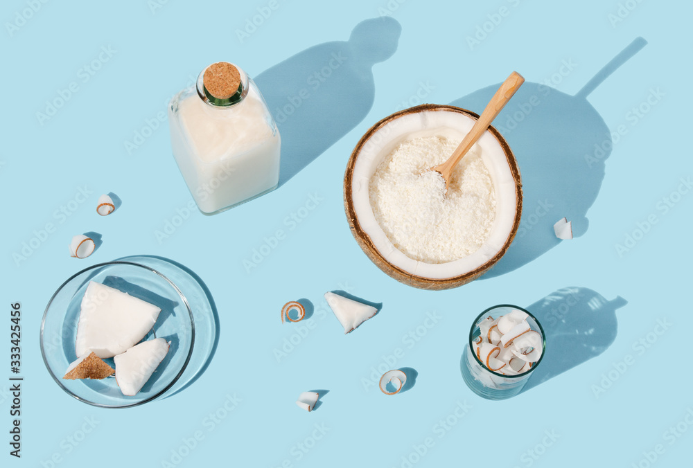 Coconut curl slices on plate, half with pulp and coconut milk oil in bottle on blue paper background Coconut curl slices on plate, half with pulp and coconut milk oil in bottle on blue paper background