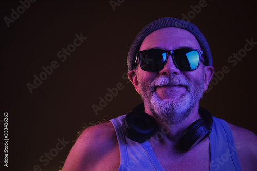 a cool aged man in hipster hat, sunglasses and tank top wearing headphones in neon light