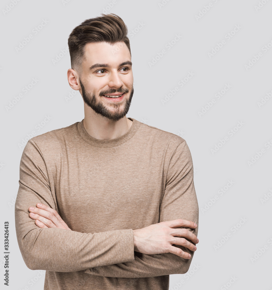 Fototapeta premium Portrait of handsome smiling young man with folded arms. Smiling joyful cheerful men with crossed hands studio shot. Isolated on gray background