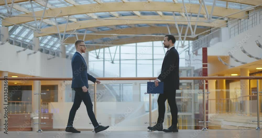 Two young male business partners shaking hands in office building Two young male business partners shaking hands in office building