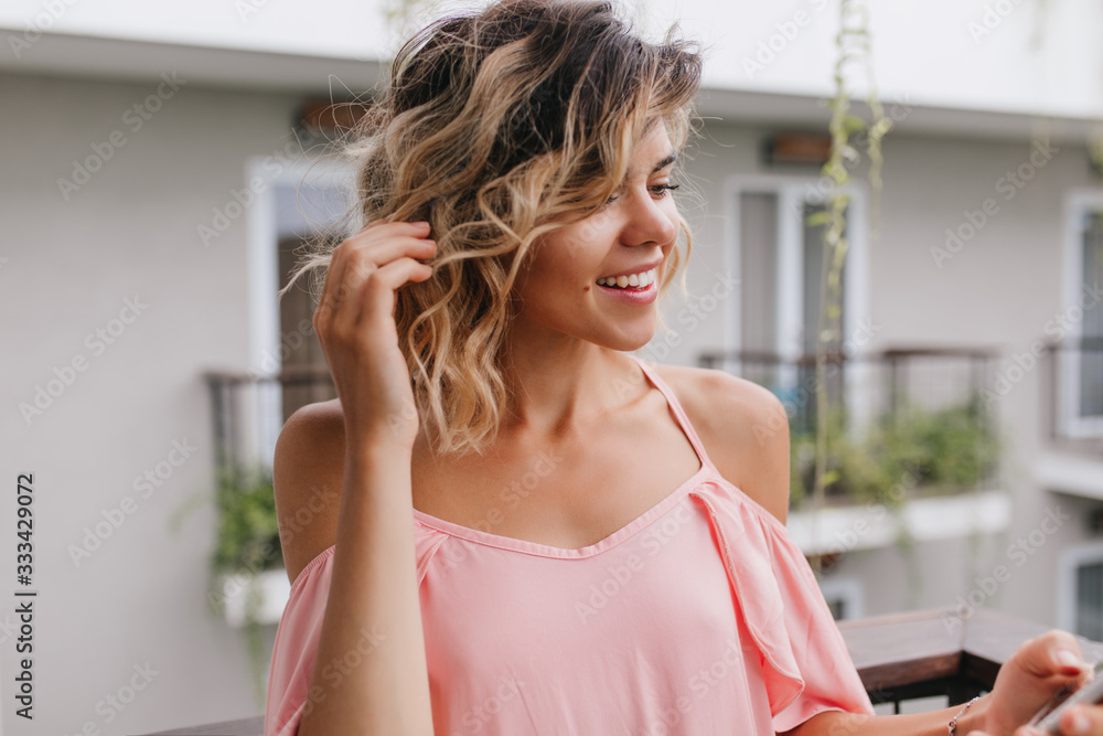 Close-up portrait of pensive woman touching her wavy hair. Outdoor photo of winsome caucasian girl posing on blur background. Close-up portrait of pensive woman touching her wavy hair. Outdoor photo of winsome caucasian girl posing on blur background.