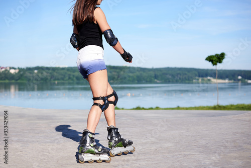 Young woman, roller-blading on rollerdrome. Tan legs, wearing roller-skates and protective equipment, showing the process of riding on metal platform.
