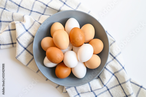 chicken eggs white and brown color in a gray plate on a checked kitchen towel on a white table. concept farm products and natural nutrition