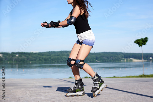 Young woman, roller-blading on rollerdrome. Tan legs, wearing roller-skates and protective equipment, showing the process of riding on metal platform. photo