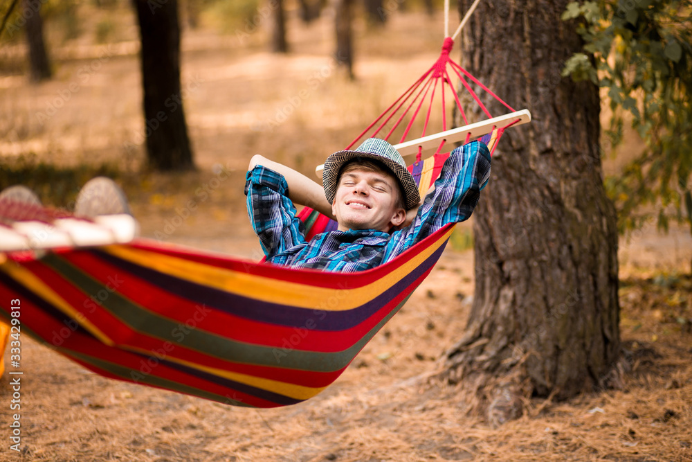 Young happy free man in hat relaxing outside in hammock in forest Young happy free man in hat relaxing outside in hammock in forest