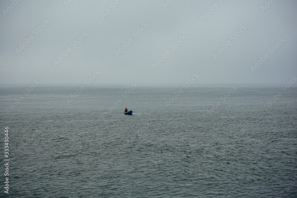 lonely fisherman in a small boat in atlantic ocean near Porto, Portugal