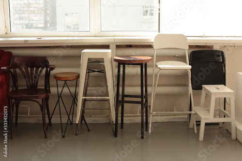 various different chairs stools stand along the wall by the window