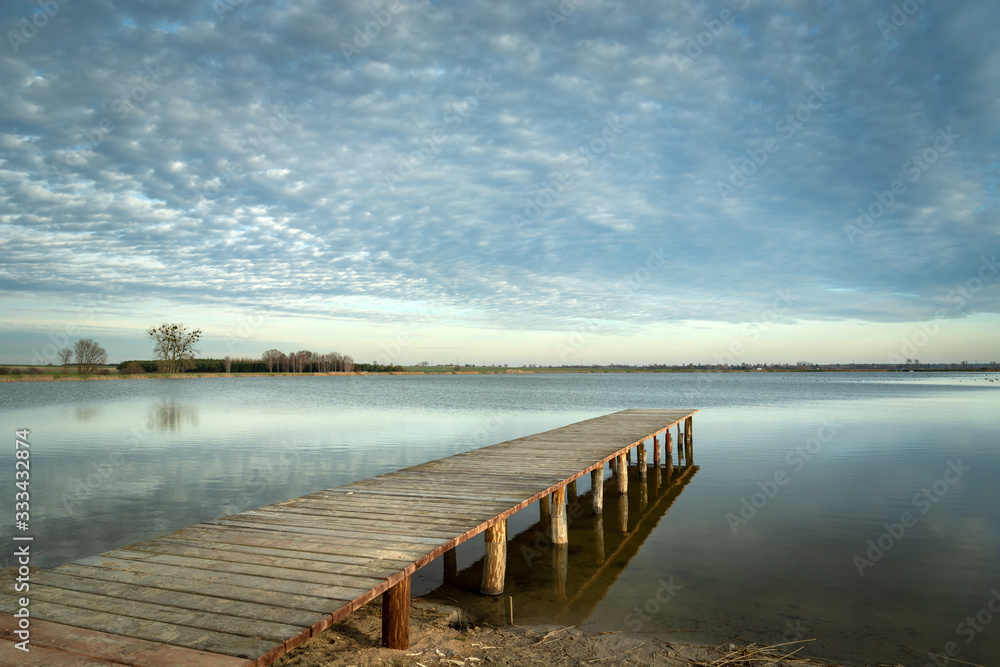 Long wooden bridge towards the lake and clouds on the sky Long wooden bridge towards the lake and clouds on the sky