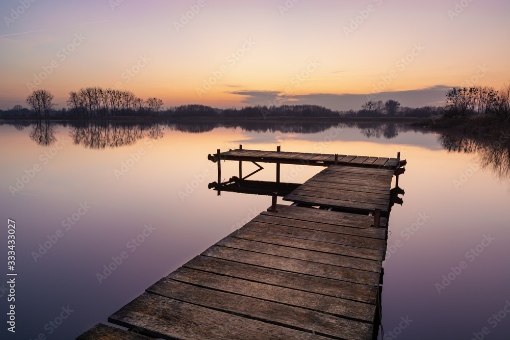 Wooden jetty and calm water surface on the lake, trees on the horizon
