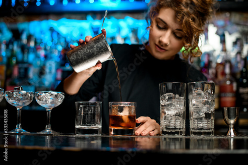 Pretty woman barman preparing cocktail and pouring it into glass.