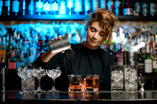 Young woman barman preparing cocktail and carefully pouring it into glass. photo