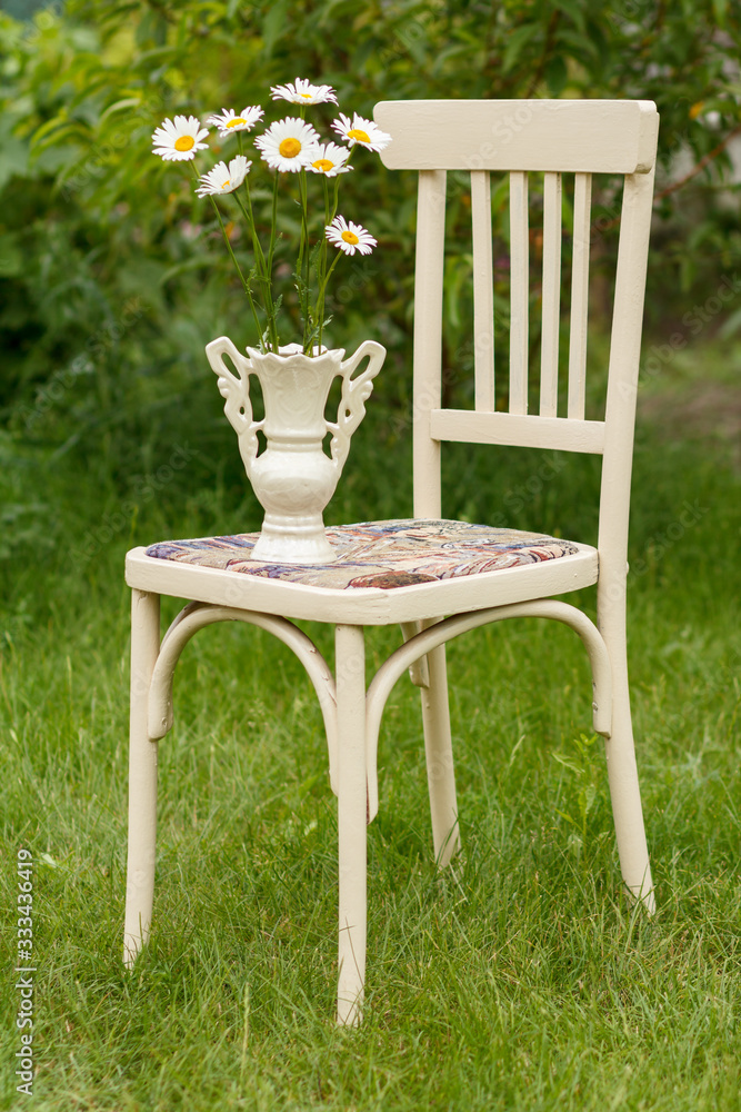 Vase with chamomile flowers on a white chair in the summer garden. Vase with chamomile flowers on a white chair in the summer garden.