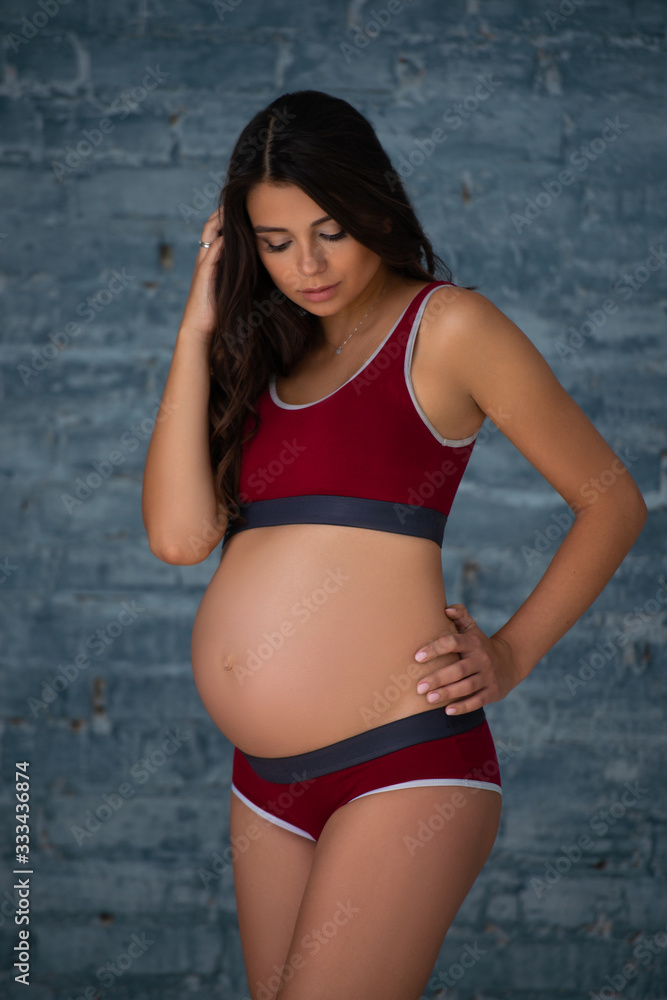 Fototapeta premium Beautiful pregnant young athletic woman in sports maternity underwear against the background of a gray brick wall