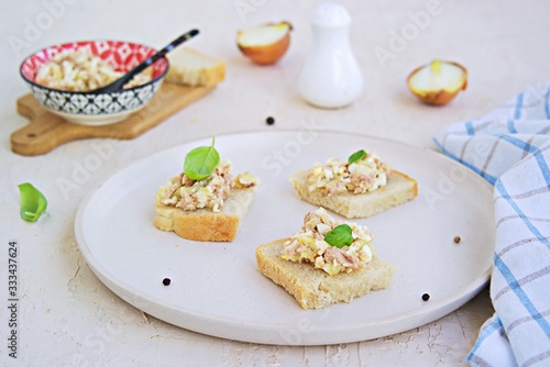 Appetizer, salad of canned cod liver, boiled egg and onion on slices of fresh white bread on a light ceramic tray. Appetizer Recipes