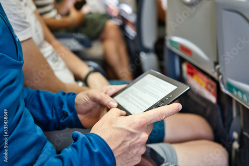 Man in a blue garment reading a book on an iBook in the seat of a low cost airplane on an air route. photo