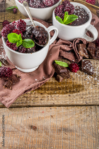 Homemade chocolate mug cake with blackberry. Breakfast easy snack recipe, chocolate non dairy cake in mugs, with blackberry, sugar powder and mint, wooden rustic background