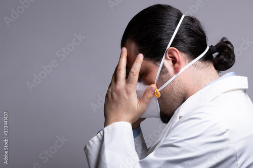 Frustrated medical doctor wearing a respiratory mask touching his head with his hands. Burnout and medicine crisis concept.