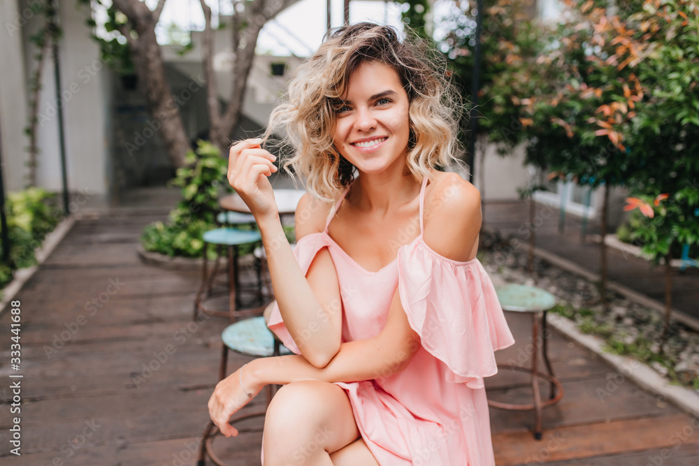 Romantic girl playing with blonde short hair while chilling in beautiful cafe. Attractive fair-haired woman posing with interested face expression in street restaurant. Romantic girl playing with blonde short hair while chilling in beautiful cafe. Attractive fair-haired woman posing with interested face expression in street restaurant.