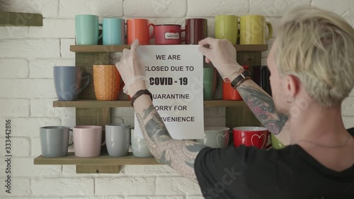 Biohazard concept of living in a new reality of coronavirus epidemic hysteria cafe owner sticks advertisement on quarantine measures to contain virus pinned on shelf with colorful mugs