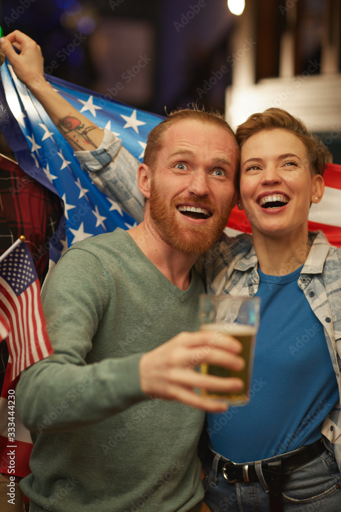 Fototapeta premium Happy young couple drinking beer and cheering for the American football team in sport bar