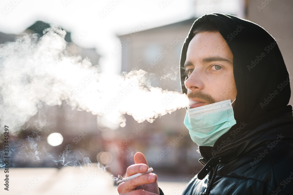 Smoking. Closeup man with mask during COVID19 pandemic smoking a cigarette at the street