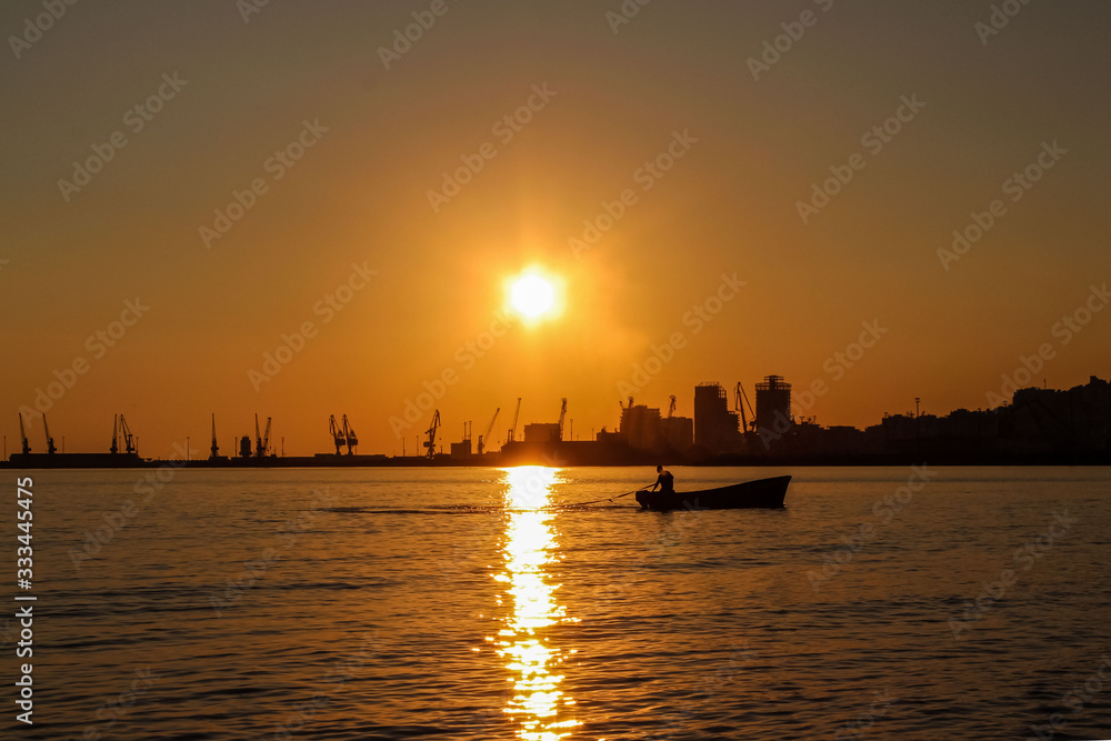 Beautiful sunset view on Port in Durres, Albania. City silhouette as background from the sea beach with fisherman fishing in a boat