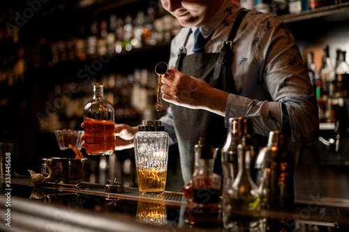 barman in black apron preparing alcoholic cocktail using shaker.