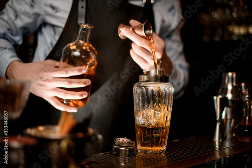 Close up. Barman carefully pours drink to glassy shaker using beaker.