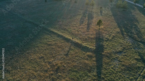 Aerial view of man traveler with backpack standing in green field. Beautiful shadows from trees. Summer sunset. Montenegro nature. Rural landscape. Countryside. photo