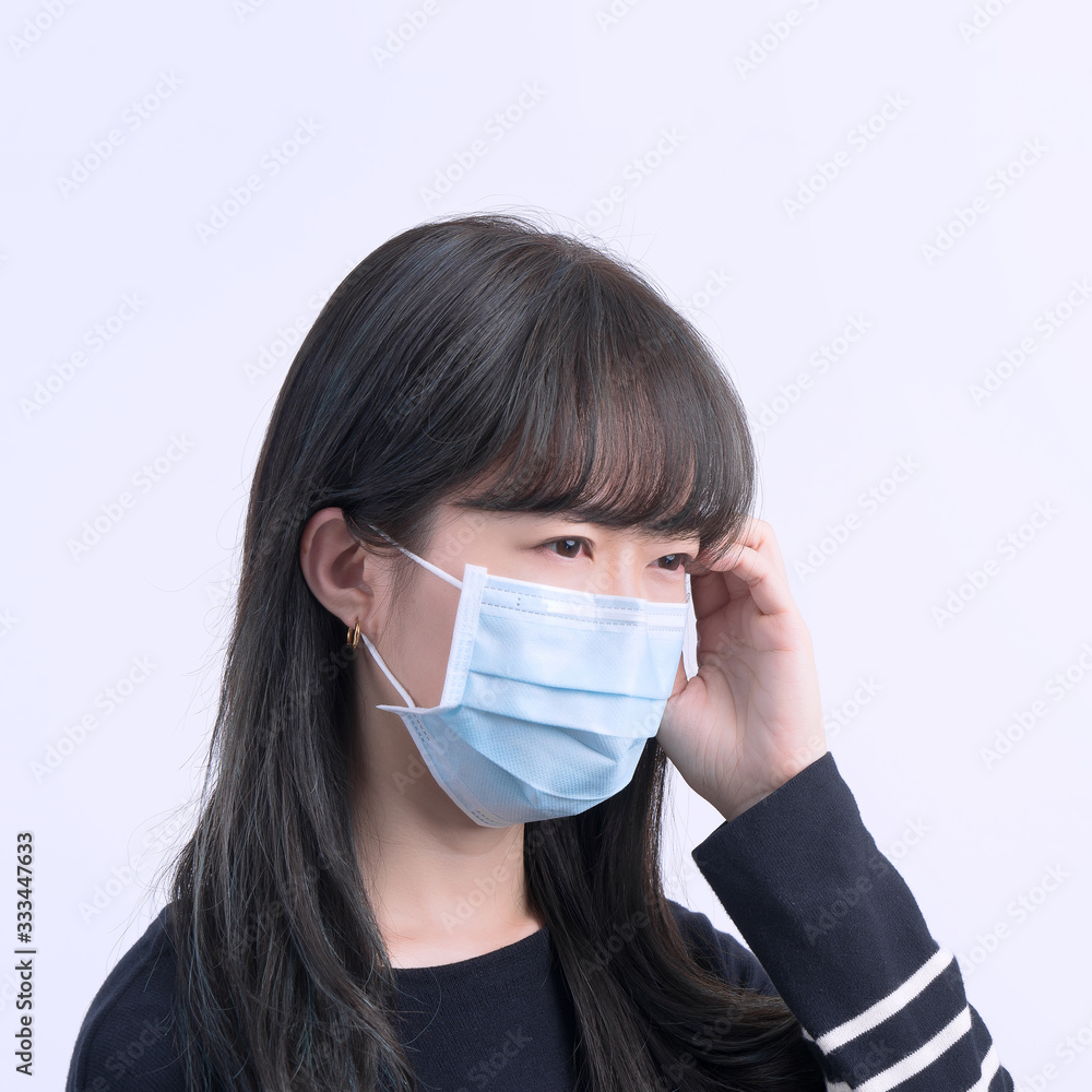 Young woman is feeling dizzy, headache, sick, unwell with wearing a medical blue face mask over the gray background, close up, copy space. Young woman is feeling dizzy, headache, sick, unwell with wearing a medical blue face mask over the gray background, close up, copy space.