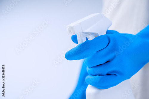 Young woman housekeeper in apron is doing cleaning with blue gloves  wet yellow rag  spraying bottle cleaner  close up  copy space  blank design concept.