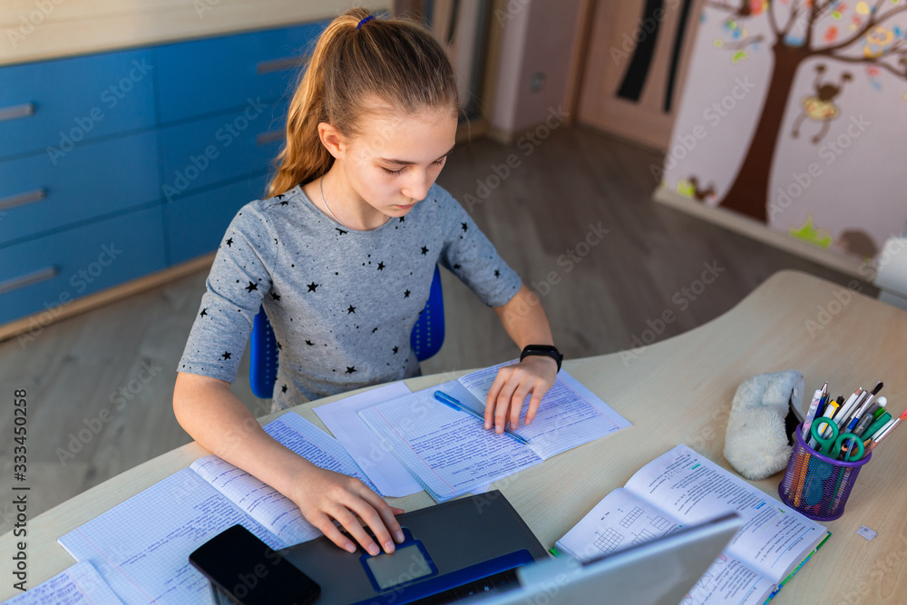 Beautiful young school girl working at home in her room with a laptop and class notes studying in a virtual class. Distance education and learning concept during quarantine Beautiful young school girl working at home in her room with a laptop and class notes studying in a virtual class. Distance education and learning concept during quarantine