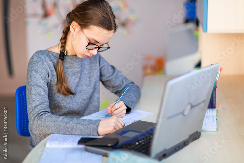 Obraz na plátně Beautiful young school girl left-handed working at home in her room with a laptop and class notes studying in a virtual class