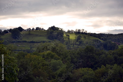 Beautiful green alpine hill, viewed from a garden. It is the evening, the sunset is beginning.