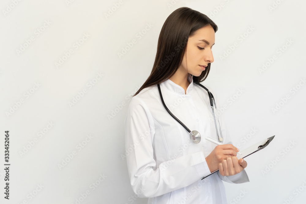 Friendly female doctor, writes the diagnosis to the clients card, a stethoscope on his neck Friendly female doctor, writes the diagnosis to the clients card, a stethoscope on his neck