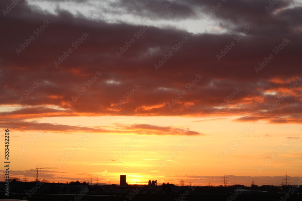 Sonnenuntergang mit dunklen Wolken, kleine Stadt mit Baukran als Silhouette Sonnenuntergang mit dunklen Wolken, kleine Stadt mit Baukran als Silhouette