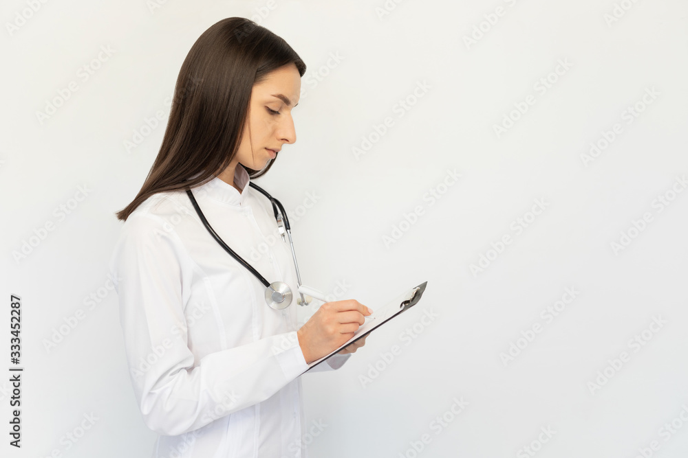 Friendly female doctor, writes the diagnosis to the clients card, a stethoscope on his neck Friendly female doctor, writes the diagnosis to the clients card, a stethoscope on his neck
