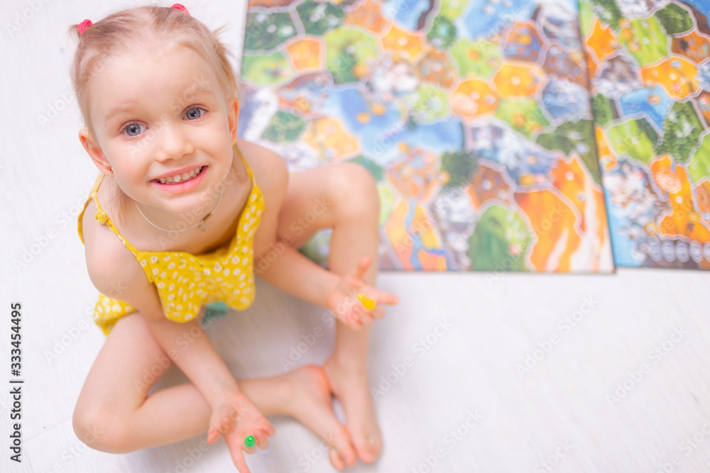 Board game concept. Little kid girl play in board game at home sitting on a wooden floor. Board game field, many figures. Board game concept. Little kid girl play in board game at home sitting on a wooden floor. Board game field, many figures.