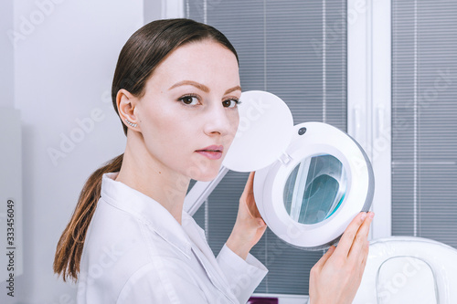 Female woman doctor is analyzing skin on face before the procedure in cabinet. Beautician cosmetology concept, presentation of anti-aging skin treatment photo