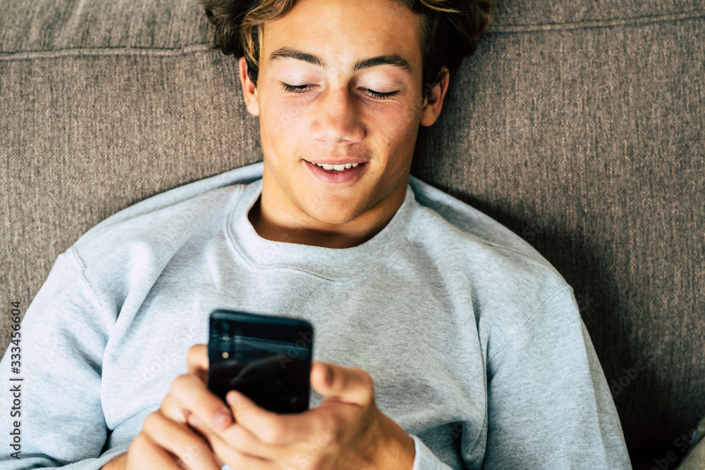 Fototapeta premium one teenager at home in quarantine using his phone and looking and revising his social network or media and playing video games on the sofa - bored man or young adult at home