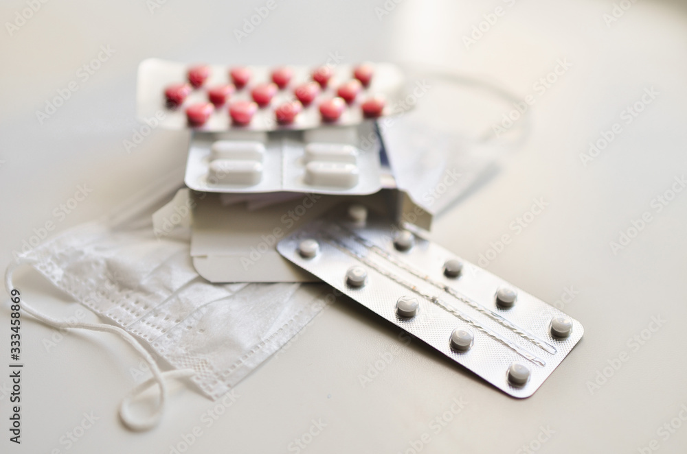 medical face mask and many different pills in blisters. Photo on a white background with bokeh. medical face mask and many different pills in blisters. Photo on a white background with bokeh.