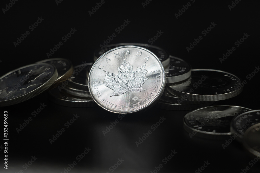 A close up of a Silver Coin leaning against a collection of coins on a black surface and background. A close up of a Silver Coin leaning against a collection of coins on a black surface and background.