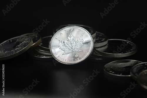 A close up of a Silver Coin leaning against a collection of coins on a black surface and background. © Denise Walker