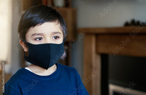 Portrait kid face wearing medical face mask, Mixed race child boy with beautiful brown eyes looking at camera black face mask, Little boy stay at home during covid-19 lock down.