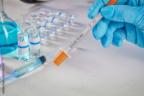 Hands in blue gloves holding testing kit. Medical flasks with colorful chemical reagents. Ampoules and syringe isolated on white. Coronavirus