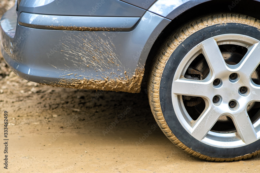 Close up of dirty car wheel with rubber tire covered with yellow mud.