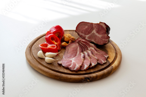 Smoked pork neck sliced together with red pepper, garlic cloves and greaves on a wooden cutting board.
