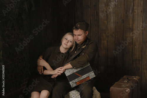 Portrait couple in military uniforms from the second world war young woman and man with accordion sit in embrace and near to them suitcase