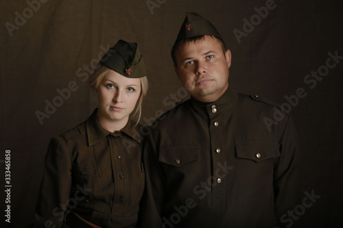 Amazing portrait young blonde woman and man in military uniform from second world war stand side by side on brown background photo